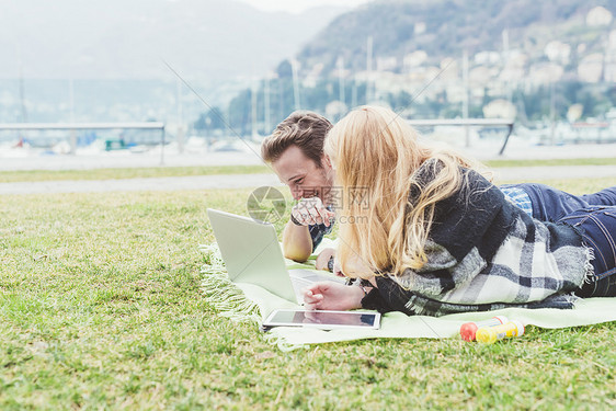 躺在野餐毯子上看笔记本电脑的年轻夫妇图片