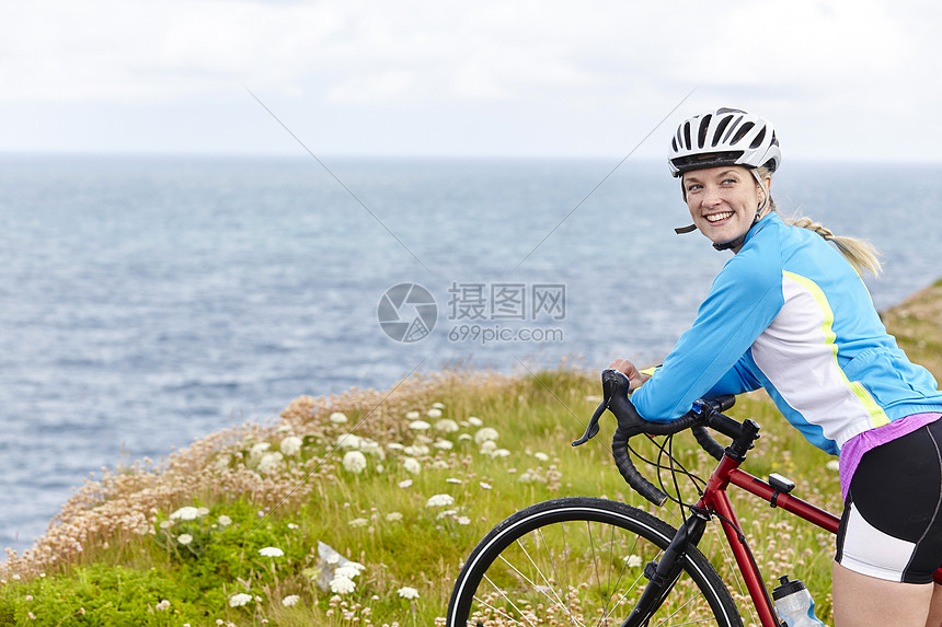 骑自行车的女人在草地山顶上放松回头微笑图片