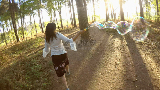 女性拿着泡泡棒在树林里奔跑图片