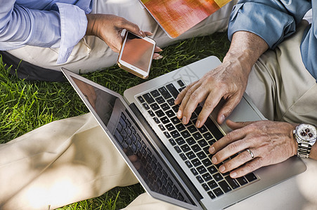 商人和妇女用坐在草地上使用笔记本电脑办公图片