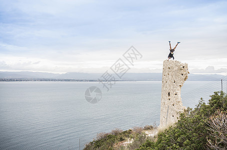 意大利卡亚里海岸被摧毁的塔台顶上做倒立的男攀岩者图片