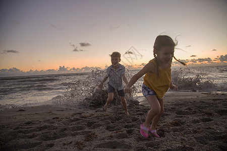 美国佛罗里达州日出时在海滩上奔跑的男孩和妹妹图片
