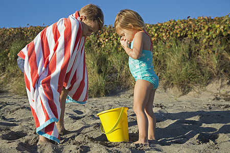 男孩用毛巾包着看玩具桶和姐妹一起在海滩上吹落岩保护区木星岛美国佛罗里达州图片