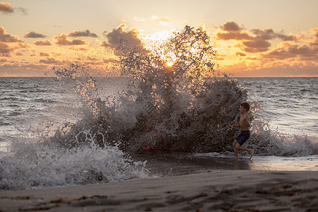 美国佛罗里达州朱庇特岛日出时男孩在飞溅的海浪中玩耍吹石头保护区图片