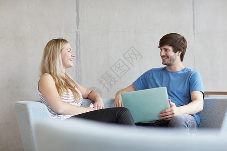 坐在学习空间沙发上用笔记本电脑的男女青年学生对视微笑图片