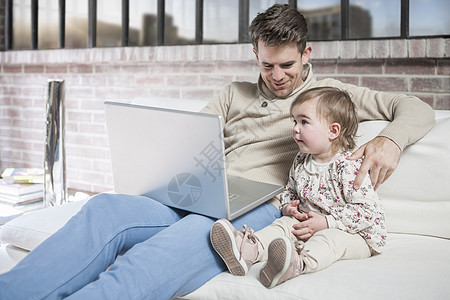 父亲坐在沙发上和年轻女儿坐在沙发上看笔记本电脑图片