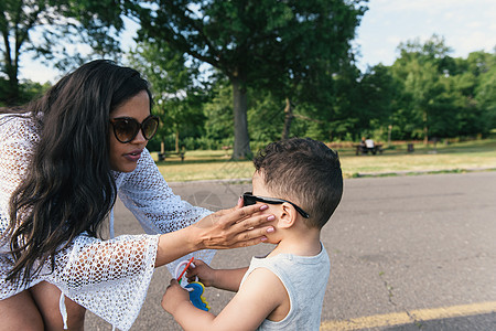妇女在美国纽约布朗克斯PelhamBay公园给小儿子戴太阳眼镜图片