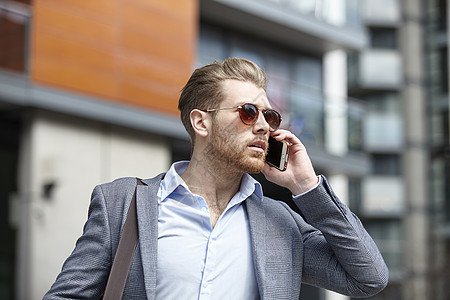 身戴太阳眼镜的青年商人在办公室外用智能手机说话联合王国伦敦图片
