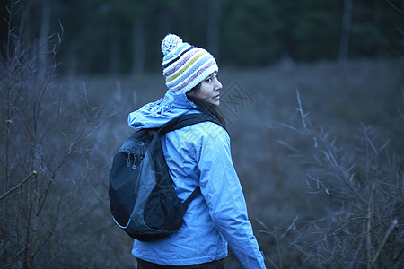 黄昏时女徒步旅行者在森林中徒步时回头看图片素材