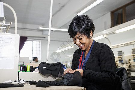 工厂女把黑布缝的线从服装厂速纫机编织的刺绣中除去图片