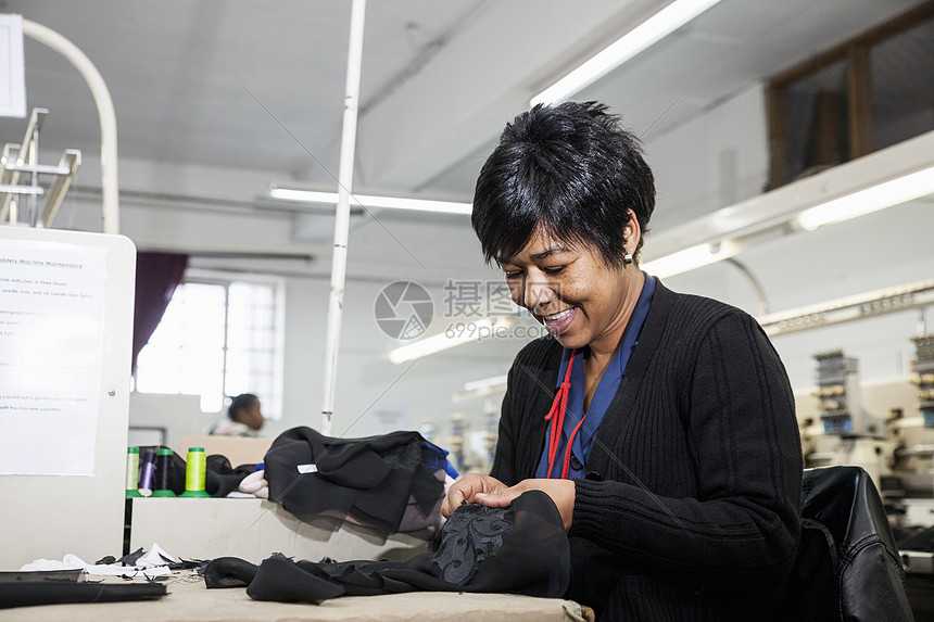 工厂女把黑布缝的线从服装厂速纫机编织的刺绣中除去图片