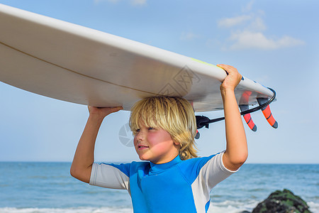 海滩上的小男孩头背着冲浪板图片