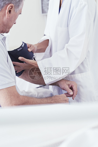 使用血压测量仪对医院床上的老年男患者进行血压测量图片