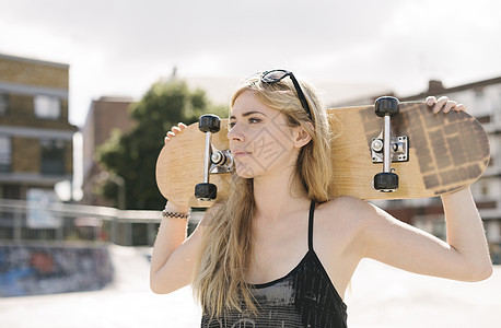 年轻女滑板运动员在冰场肩膀上携带滑板图片