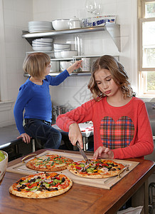 两个年轻女孩在厨房切披萨图片