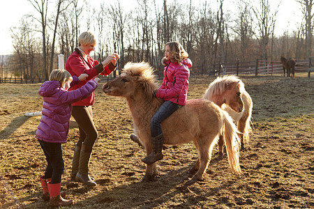 女孩骑着小马母亲和姐妹站在她们身边图片素材