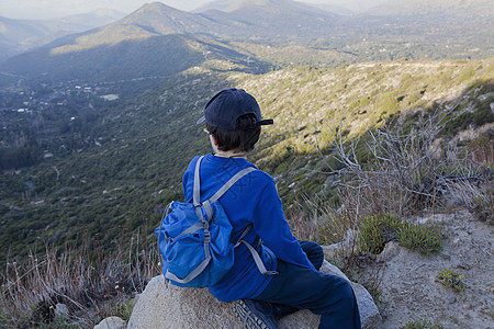 小男孩坐在巨石上看着智利瓦尔帕莱索的安第斯山图片