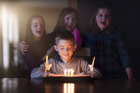 男孩被朋友包围看着生日蛋糕微笑图片