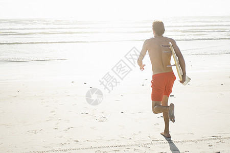 海滩上拿着冲浪板跑的年轻男人图片
