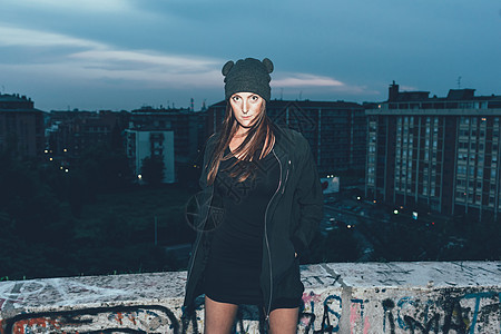 夜间在城市顶楼戴着编织帽的年轻女性肖像图片
