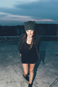 夜间在城市顶楼戴着编织帽的年轻女性肖像图片