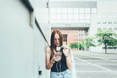 年轻女靠在墙上阅读智能手机短信图片