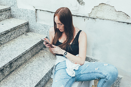 坐在楼梯上阅读智能手机短信的年轻妇女图片