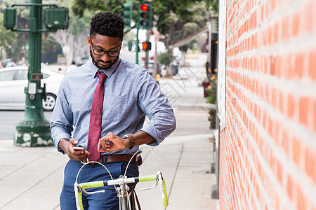 年轻人站在自行车旁边使用智能手机看表图片