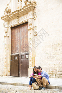 情侣两人坐在人行道旁使用移动电话图片