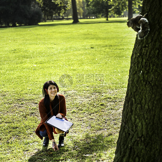 年轻姑娘在公园里蹲着看树上的松鼠图片