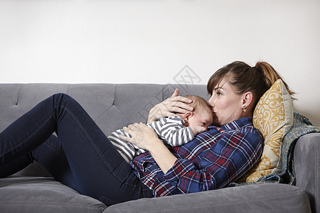 母亲躺在沙发上的亲吻男婴的前额图片