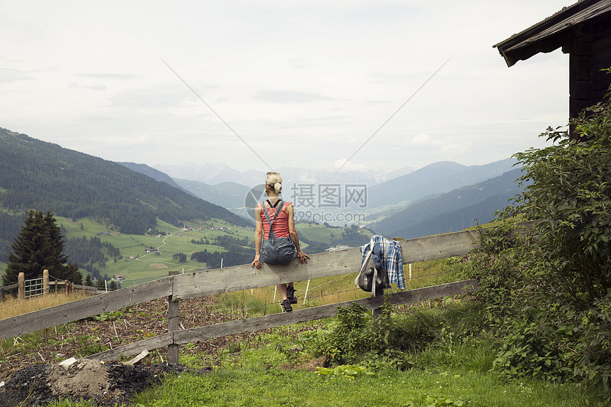 坐在栅栏上望向山地的妇女后视力奥地利蒂罗尔萨特伯格姆图片