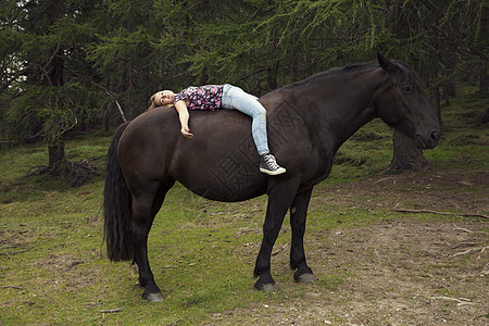 奥地利提罗尔州Sattelbergalmalm的森林角上躺在马背的女孩图片