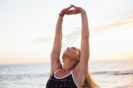在沙滩扶起的手臂上做伸展运动的妇女图片