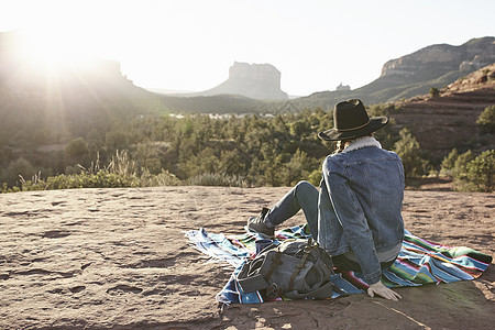 美国亚利桑那州塞多纳市一名妇女坐在沙漠中的毯子上看着风景后视图图片