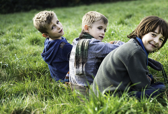秋天三个男孩坐在一起野外的田野上图片