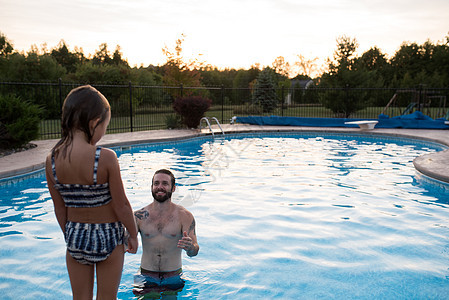 站在游泳池边缘的年轻女孩父亲在游泳池鼓励她跳进游泳池图片