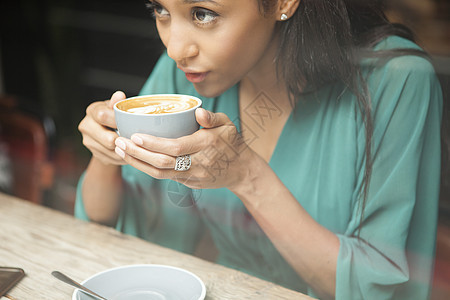 中等成年妇女拿着咖啡杯向厅窗外看图片