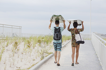 美国纽约州罗克韦海滩一对年轻夫妇头顶着冲浪板的背影图片