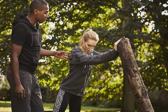 公园里年轻女子在个人教练的帮助下举树干图片