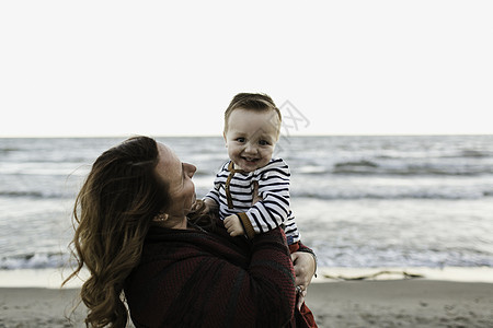 母亲在海滩上抱着微笑的男孩儿图片