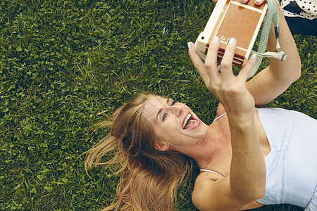 躺在草地上的年轻女人用反光相机拍自图片