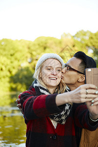 一对夫妇在公园湖边使用智能手机自拍图片