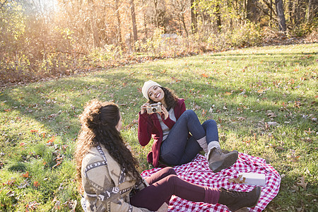 野餐毯子上的女青年给朋友拍照图片