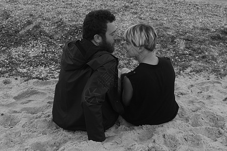 坐在沙滩上面对面的年轻夫妇后视图片