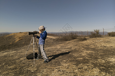男孩通过三脚架上的望远镜看远方图片