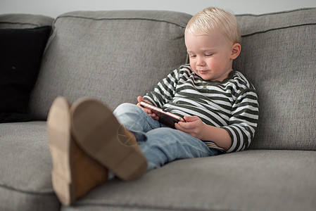 小男孩躺在沙发上玩手机图片