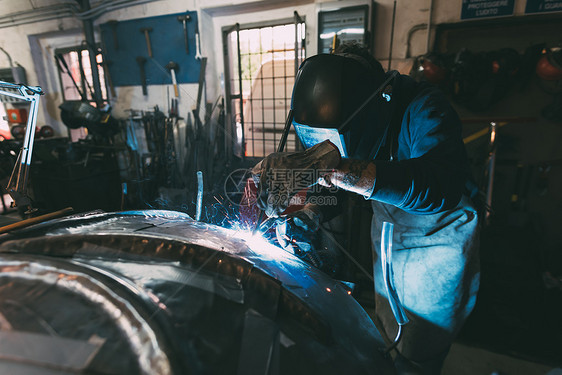 带着焊接面罩在金属铸造车间焊接金属的工人图片