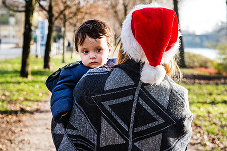 在公园里戴着圣诞帽的年轻女人抱着婴儿男孩图片
