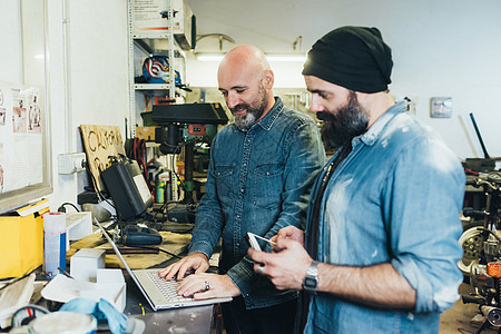 两个成熟男子在车库用笔记本电脑工作图片